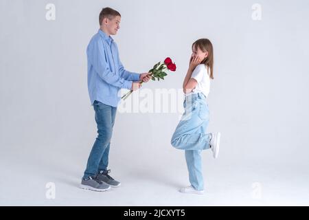 Teen boy dà alla sua ragazza un bouquet di rose rosse su sfondo bianco. Primo concetto di amore. Fotografia da studio. Foto Stock