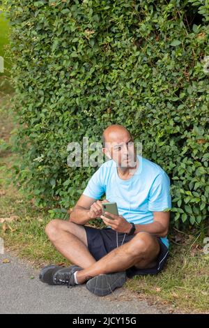 L'uomo calvo si stanca dopo una dura giornata di sport facendo una pausa per prendere il respiro mentre ascolta la musica Foto Stock