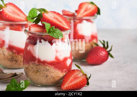 Cheesecake alla fragola. Cheesecake o trifle con fragola in vetro su sfondo vecchio tavolo grigio cemento. Cheesecake senza cottura. Dess Foto Stock