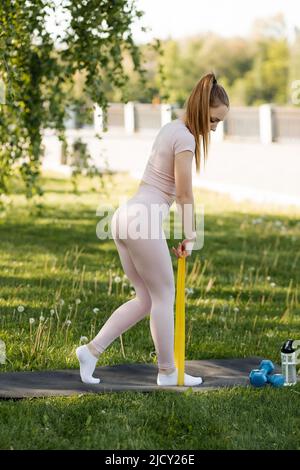 Ragazza con fascia elastica in gomma che si allena alle braccia e alla  schiena all'aperto nel parco. Giovane donna che si allena al mattino con  attrezzature aggiuntive, vista dal retro Foto stock 