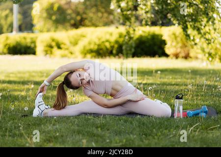 Ragazza atletica che fa un riscaldamento su un materassino fitness nel parco Foto Stock