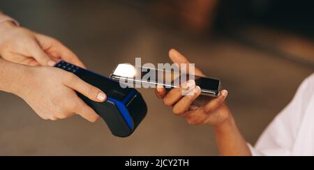 Cliente irriconoscibile che esegue la scansione del suo smartphone su una macchina con carta di credito per pagare la sua fattura in un bar. Donna che fa una transazione senza contanti e contactless Foto Stock