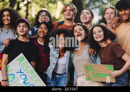 Gruppo di adolescenti multiculturali sorridenti felicemente mentre si levano in piedi insieme ad una protesta di cambiamento climatico. Diversi attivisti giovanili che si uniscono al clima globale Foto Stock