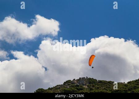 Tandem arancione parapendio contro un cielo blu nuvoloso, giorno di sole Foto Stock