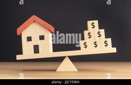 Concetto di investimento immobiliare o di casa. Modello di casa e blocchi di legno con il segno del dollaro che bilancia su un seesaw Foto Stock