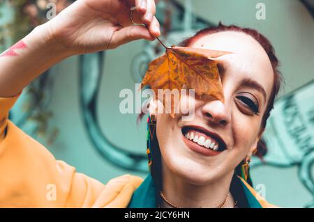 bella giovane latino argentina donna ridendo copre un occhio con una foglia asciutta autunno, in piedi guardando la macchina fotografica felice e divertente. Foto Stock