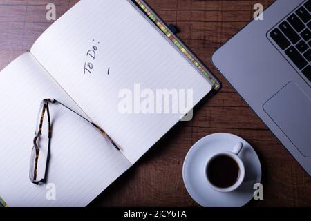 Tavolo in legno con computer, caffè espresso in una tazza bianca su una pentola bianca, bicchieri, penna e notebook. Foto Stock