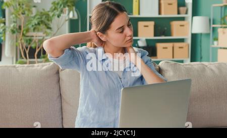 Freelancer seduto sul divano lavoro a distanza da casa improvvisamente sensazione di dolore alla schiena e alla vita. Donna sensazione stanca di lungo sedentary Lifestyle provare Foto Stock