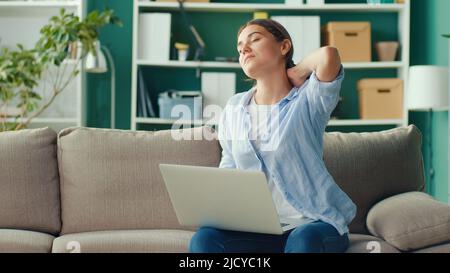 Freelancer seduto sul divano lavoro a distanza da casa improvvisamente sensazione di dolore alla schiena e alla vita. Donna sensazione stanca di lungo sedentary Lifestyle provare Foto Stock