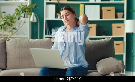 Freelancer seduto sul divano lavoro a distanza da casa improvvisamente sensazione di dolore alla schiena e alla vita. Donna sensazione stanca di lungo sedentary Lifestyle provare Foto Stock