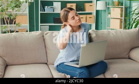 Freelancer seduto sul divano lavoro a distanza da casa improvvisamente sensazione di dolore alla schiena e alla vita. Donna sensazione stanca di lungo sedentary Lifestyle provare Foto Stock