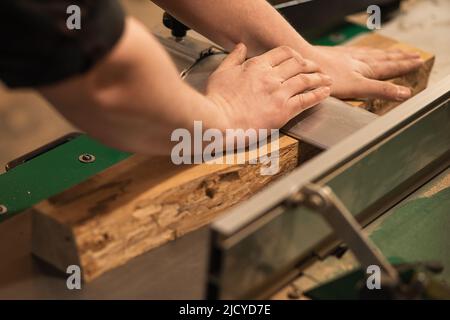 Primo piano di carpentiere, operatore di falegname, pressione, abbassamento, messa in tavola di legno sulla macchina da taglio in officina Foto Stock