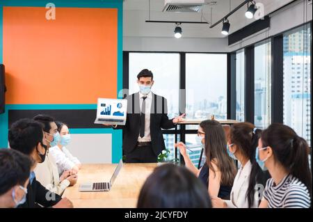 Uomo d'affari caucasico esecutivo indossare maschera con presentazione di business plan da portatile, incontro d'affari aziendale con colleghi multietnici Foto Stock