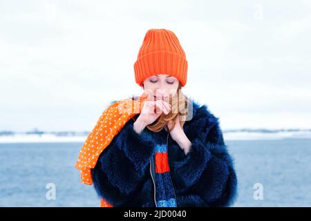 Ritratto attraente Girl Walk in Winter Park su sfondo neve inverno. Giovane donna felice in elegante vestito caldo e berretto arancione Beanie. Tempo ventoso Foto Stock