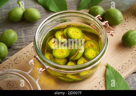 Macerando le noci non mature tagliate a fettine in alcol in un vasetto, per preparare il liquore fatto in casa Foto Stock