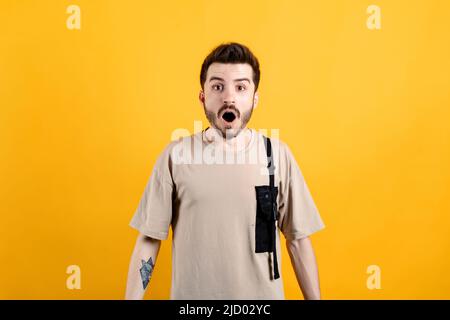Ritratto di giovane uomo caucasico con t-shirt in posa isolato su sfondo giallo paura e scioccato con sorpresa e stupito espressione, paura e Foto Stock