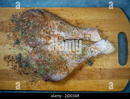 Bastoncini di tacchino in spezie giacciono su un tagliere da cucina. Carne di pollame. Gamba di tacchino. La carne succosa aspetta di essere cucinata. In attesa del forno. Prosciutto Foto Stock