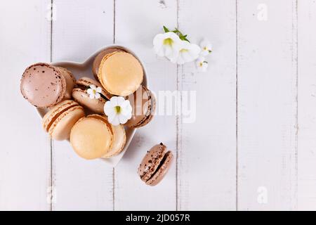 Macaron francese di colore marrone naturale, beige e crema su piatto a forma di cuore con spazio copia Foto Stock