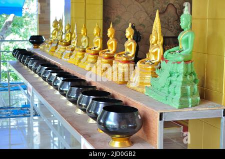 Statue di Buddha seduti in Thailandia e fila di alme-ciotole nel tempio buddista per donare denaro dalle preghiere buddiste. Foto Stock