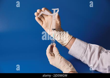 La mano guantata tenendo la siringa su sfondo blu Foto Stock