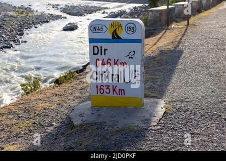 Dir, KPK, Pakistan - Giugno, 11, 2022: Segnaletica stradale pietra con informazioni sulla destinazione in chilometri scritto in inglese e traduzione Urdu Foto Stock