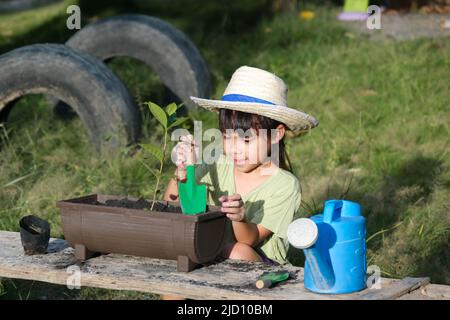 La bambina che indossa un cappello aiuta la madre nel giardino, un piccolo giardiniere. Cute ragazza piantando fiori in pentole per la vendita. Famiglia piccola impresa Foto Stock