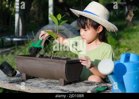 La bambina che indossa un cappello aiuta la madre nel giardino, un piccolo giardiniere. Cute ragazza piantando fiori in pentole per la vendita. Famiglia piccola impresa Foto Stock