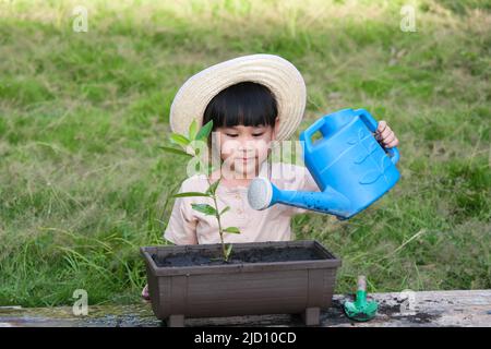 La bambina che indossa un cappello aiuta la madre nel giardino, un piccolo giardiniere. Cute ragazza piantando fiori in pentole per la vendita. Famiglia piccola impresa Foto Stock