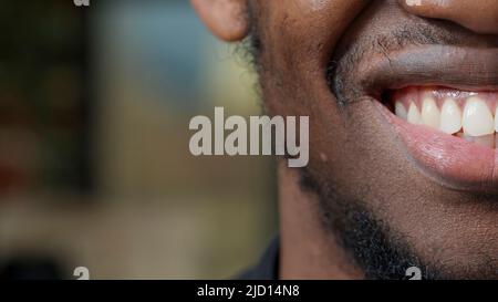 Macro scatto del giovane uomo muovendo le labbra e sorridendo, mostrando metà del volto sulla fotocamera. Buon attraente adulto con sorriso candido, denti bianchi e rifilatura del pane pulito sul mento. Emozioni autentiche. Primo piano. Foto Stock