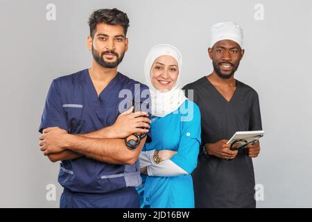 Gruppo di paramedici sorridenti su sfondo grigio. donna medico musulmana con colleghi chirurgo africano e indiano Foto Stock