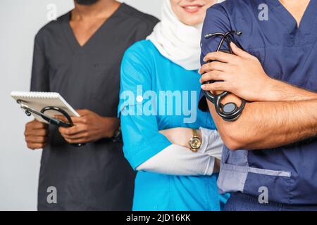 Gruppo di paramedici sorridenti su sfondo grigio. donna medico musulmana con colleghi chirurgo africano e indiano Foto Stock