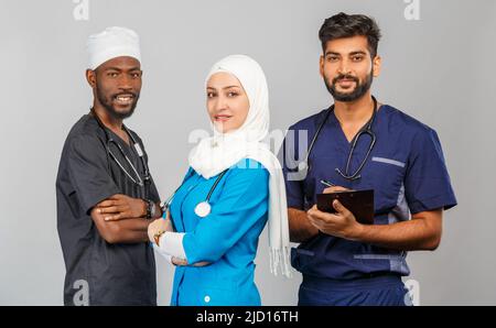 Gruppo di paramedici sorridenti su sfondo grigio. donna medico musulmana con colleghi chirurgo africano e indiano Foto Stock