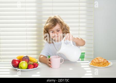 Bambino carino che versa latte intero di mucche. Ragazzo che mangia verdure alimentari sane. Colazione con latte, frutta e verdura. Bambini che mangiano durante il pranzo o. Foto Stock