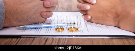 Accoppiare la mano con il divorzio accordo e Golden gli anelli di nozze sulla scrivania in legno Foto Stock