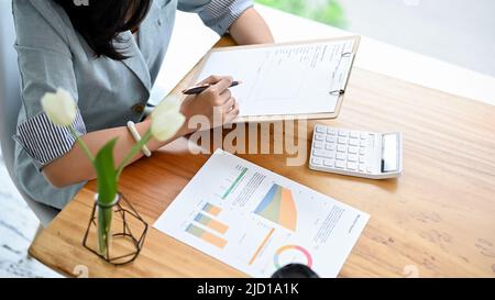 Vista dall'alto, Una donna d'affari che legge un documento di affari, controlla o rivede un rapporto finanziario alla sua scrivania dell'ufficio. Foto Stock