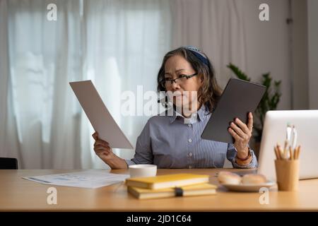 Sorridente donna asiatica anziana con tablet digitale a casa. Concetto di lavoro da casa. Foto Stock