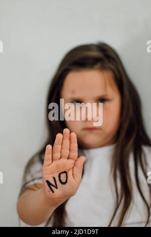 ritratto di piccola ragazza livida alzando la mano per coprire la bocca, mostrando l'iscrizione no sulla palma. Verticale. Foto Stock