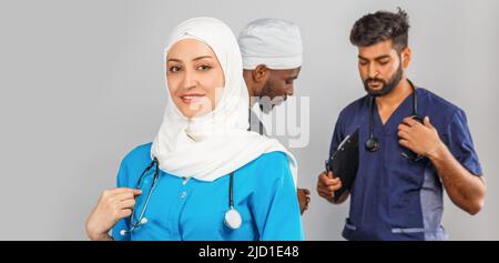 Gruppo di paramedici sorridenti su sfondo grigio. donna medico musulmana con colleghi chirurgo africano e indiano Foto Stock