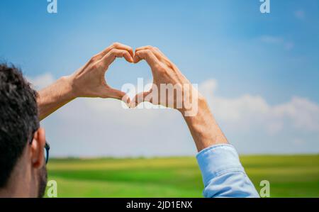 Le mani si uniscono a forma di cuore, le mani dell'uomo a forma di cuore, le mani che formano un cuore nel campo, il concetto di persona che crea Foto Stock