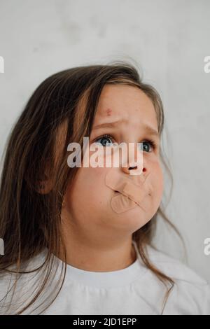 ritratto di piccola ragazza contusa con capelli lunghi che chiedono aiuto. Sigillato in bocca con cerotti medici. Foto Stock