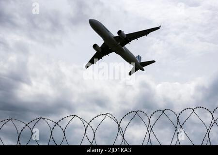 Aereo che decolla contro un cielo nuvoloso scuro, recinzione di sicurezza, filo spinato, Stoccarda, Baden-Wuerttemberg Foto Stock