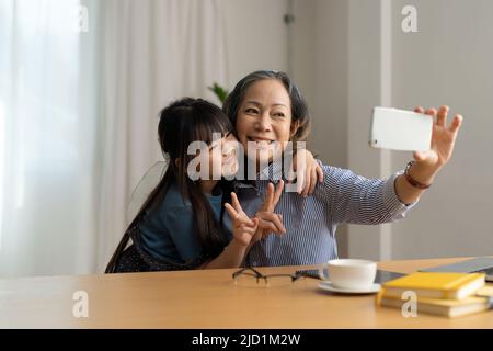 Felice asiatico sorridente nonna più anziana e bambina che si diverte a prendere selfie al telefono, allegro nonna con piccolo gioco di bambini fare foto su cellulare Foto Stock