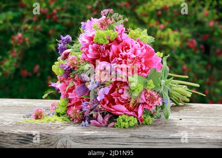 Bouquet colorato di fiori in tonalità rosso, rosa e viola con peonie e colonne, sdraiato su tavola di legno intemperie in giardino Foto Stock