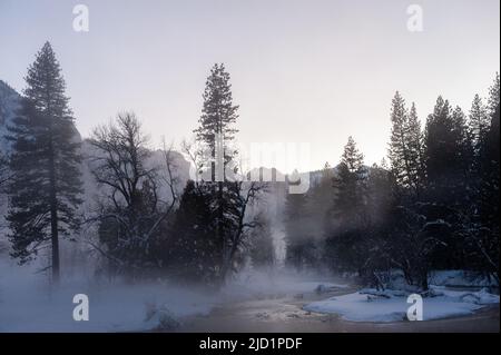 La valle di Yosemite è circondata da un sottile strato di nebbia che si estende sul fiume merced, fornendo un'atmosfera inquietante intorno al tramonto. Foto Stock