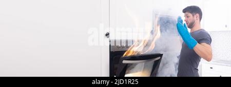 Paura giovane uomo Guardando il fuoco che esce dal forno in cucina Foto Stock