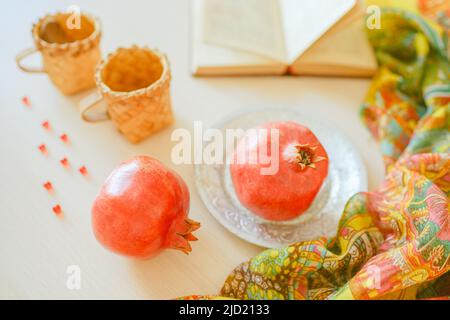Melagrane intere in piatto, libro di cucina aperto, vitamine e tazze sul tavolo. Foto Stock