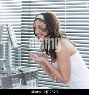 la giovane donna creme il viso e cura la pelle nel suo bagno Foto Stock
