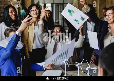 Le imprese multietniche celebrano il successo dei progetti di energia rinnovabile insieme lanciando documenti in ufficio - Focus sui mulini a vento Foto Stock