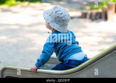 vista posteriore del bambino sullo scivolo, ragazzo di un anno che usa lo scivolo sul parco giochi Foto Stock