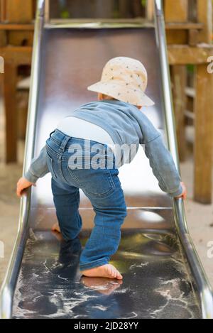 vista posteriore del bambino che sale sullo scivolo, bambino di un anno che usa lo scivolo sul parco giochi Foto Stock